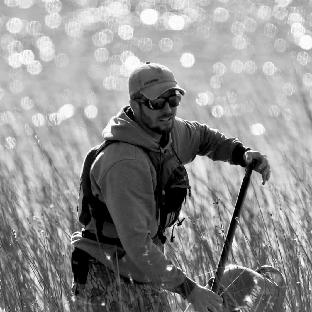 A man in the tall grass with a fishing pole.