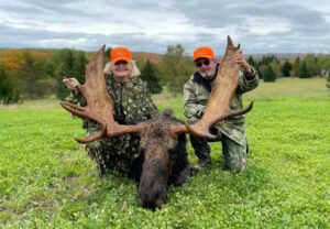Two men posing with a large moose in the grass.