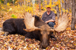 A man sitting next to a moose in the woods.