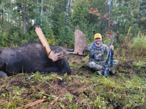 A man holding an arrow and sitting next to a moose.