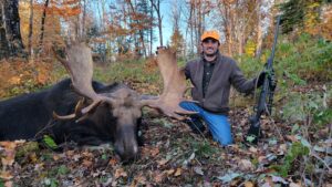 A man kneeling down next to a large moose.