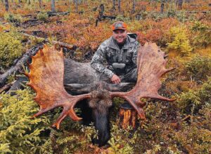 A man sitting in the grass with his moose.