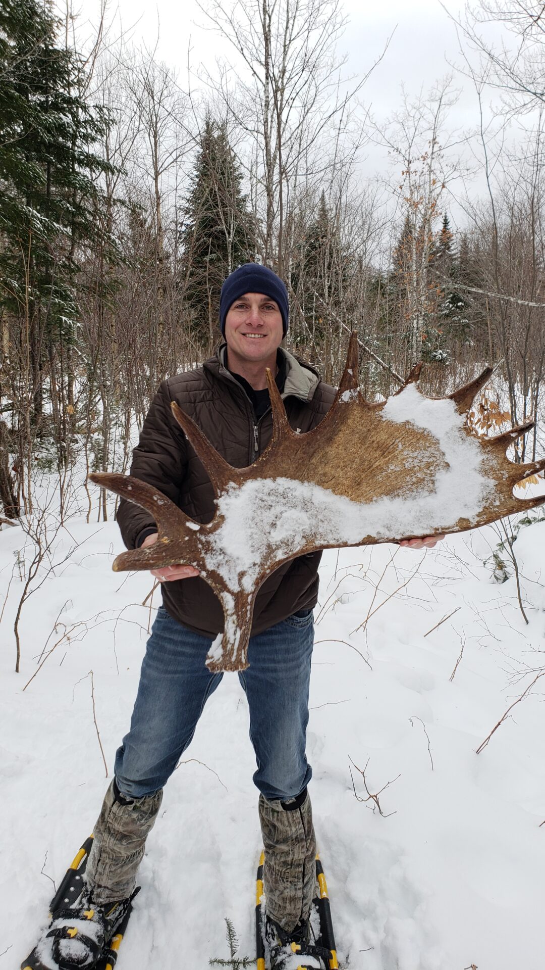 Man in snowshoes holding a moose antler.