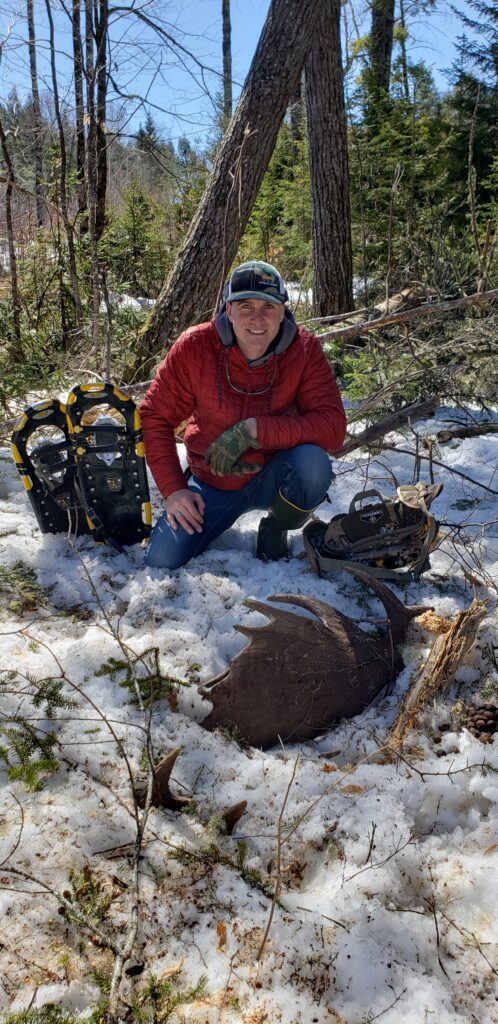 Man in red jacket with antlers and snowshoes.