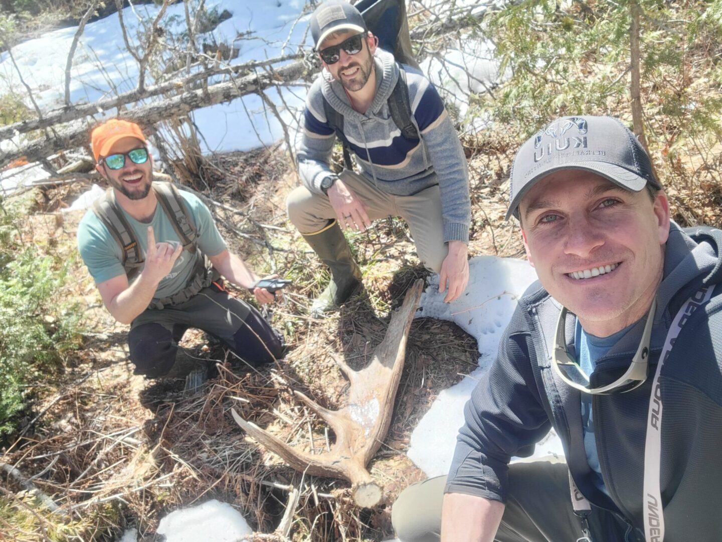 Three men pose with a moose antler.