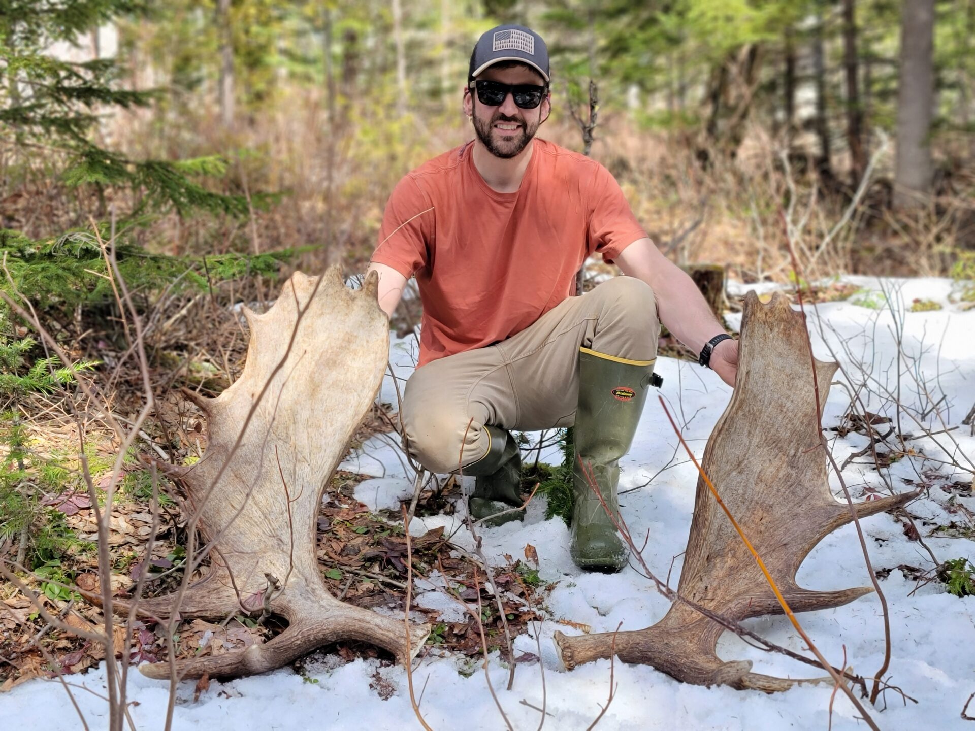 Man kneeling with two large moose antlers.