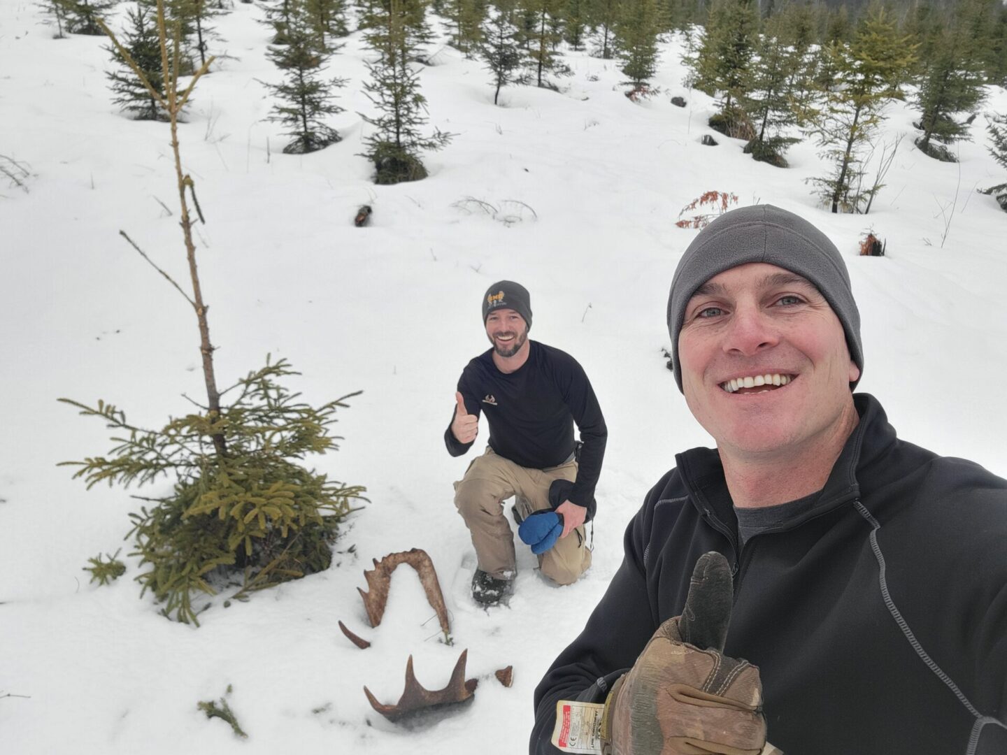 Two men smiling with moose antlers in snow.