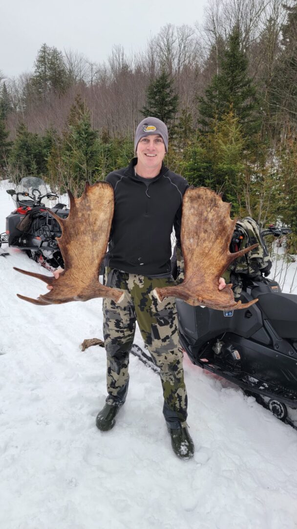 Man holding large moose antlers in snow.