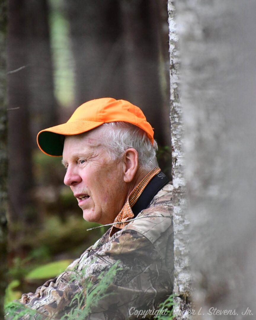 Older man in camouflage and orange hat.