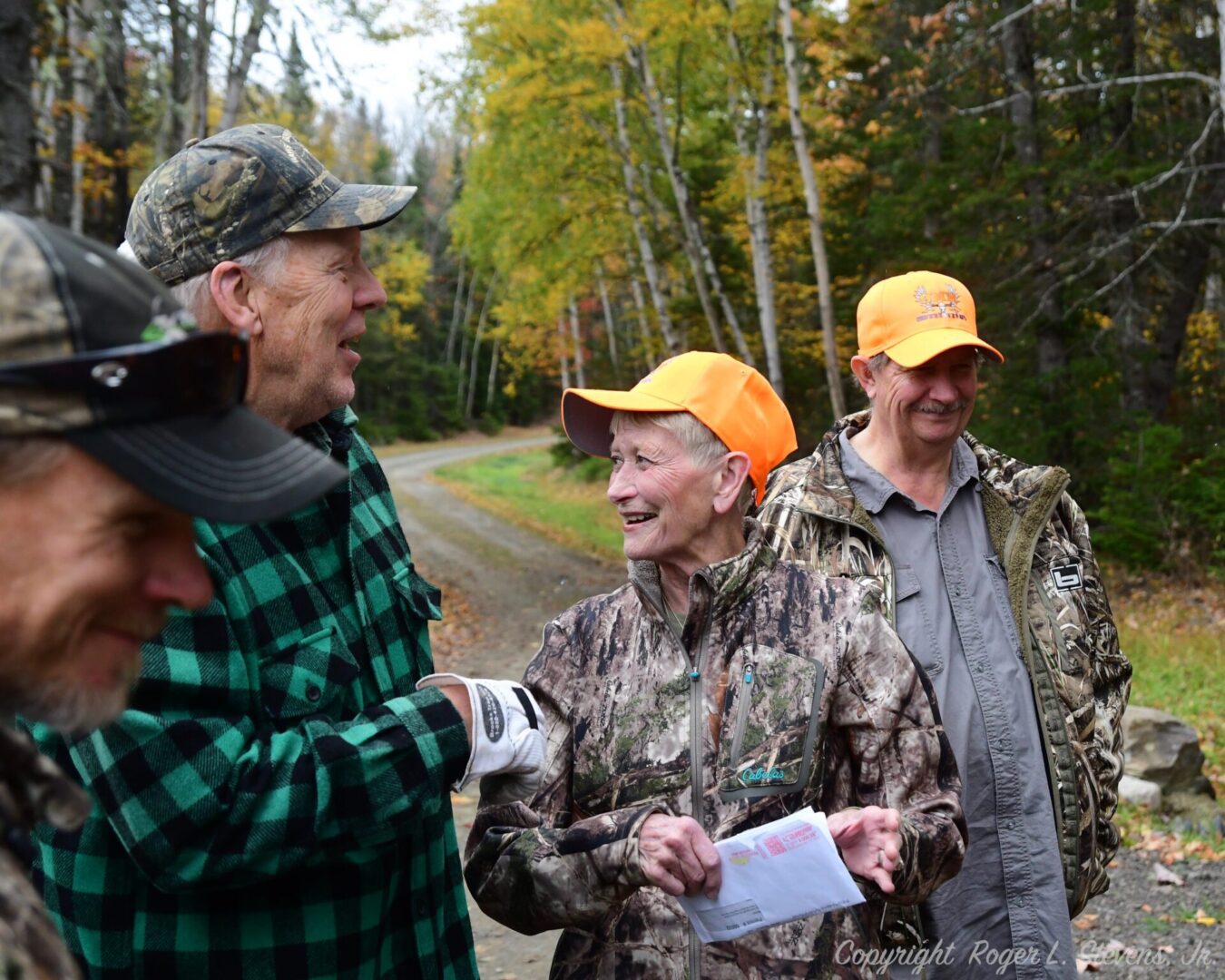 Three people in camo in the woods.