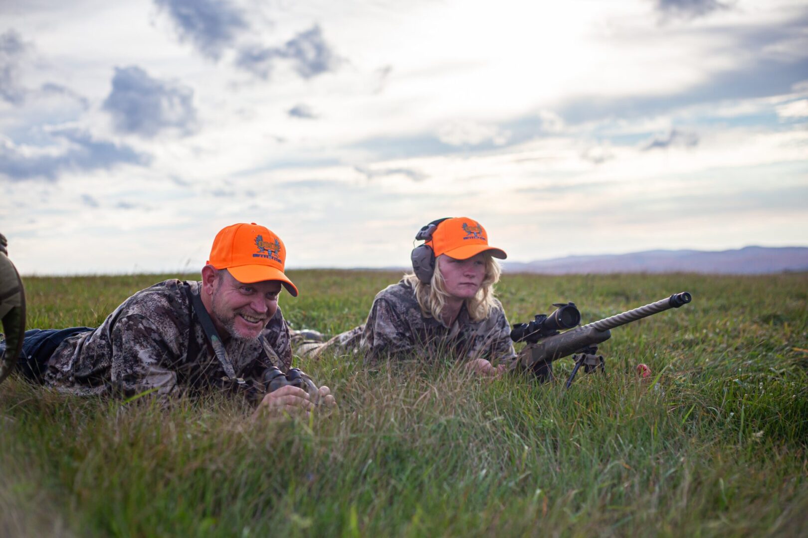 Two hunters with a rifle in tall grass.