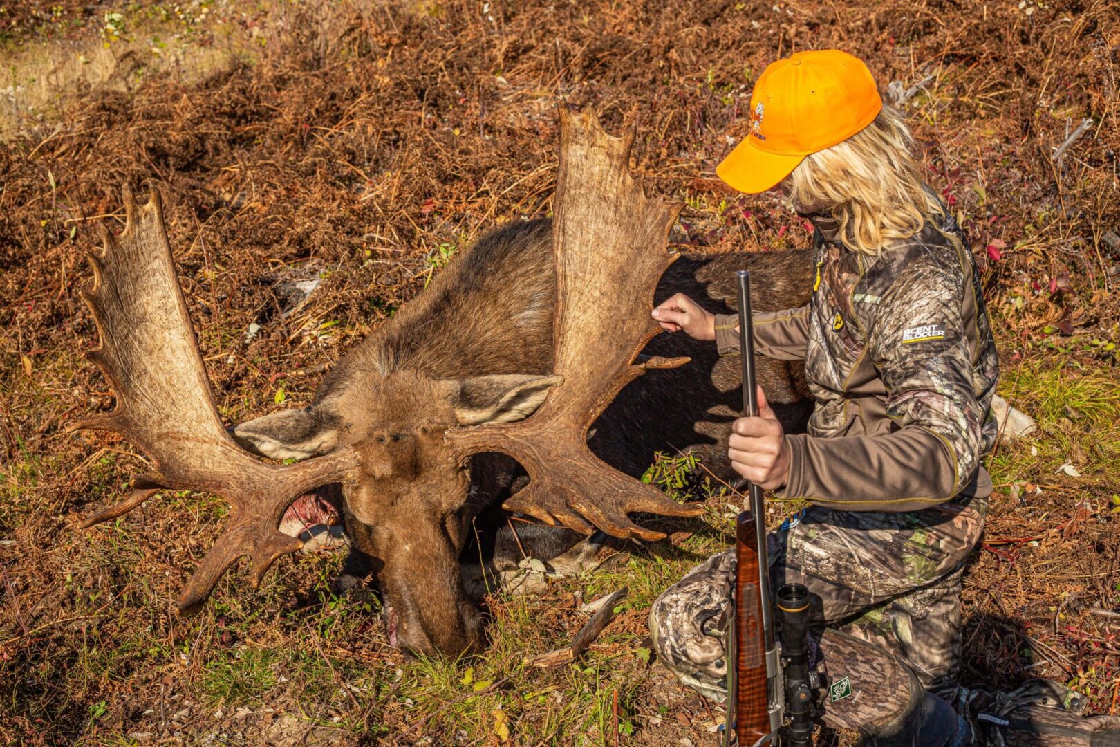 Hunter with a rifle next to a moose.