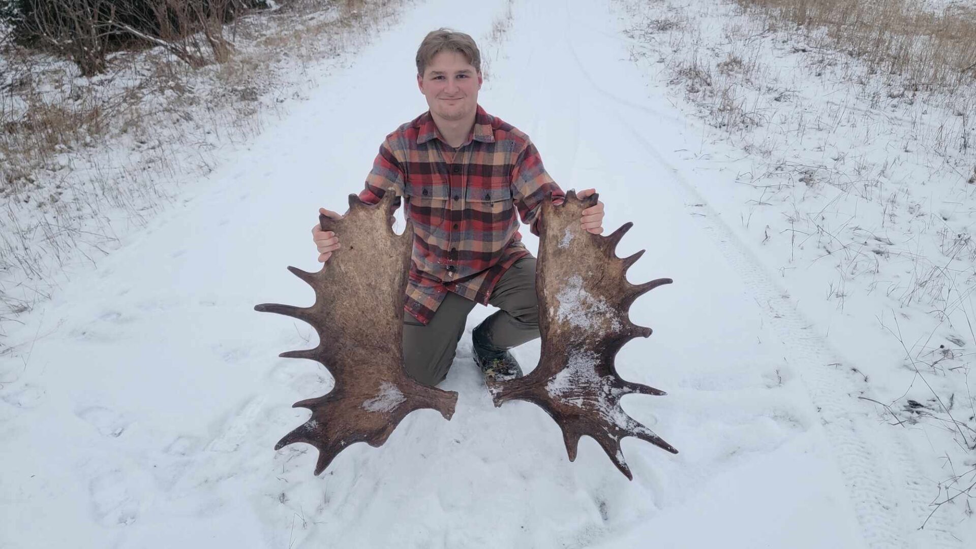 Man holding large moose antlers in snow.