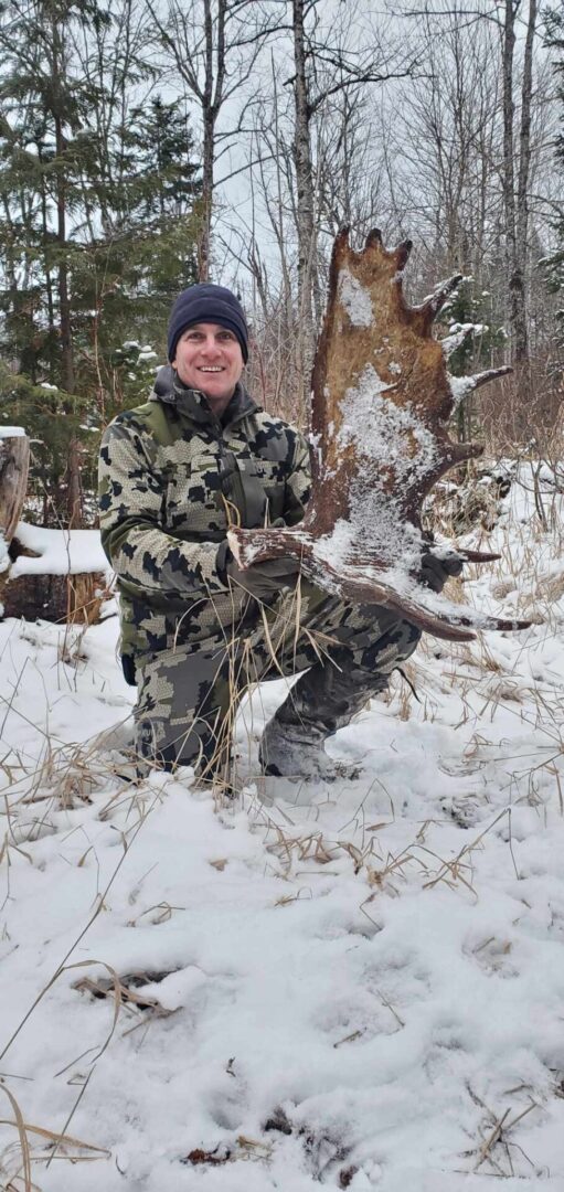 Man holding a large moose antler in snow.